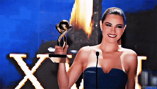 a woman in a blue dress is holding a trophy in front of a sign that says xxi