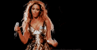 a woman in a gold dress is holding a pizza and a microphone on a stage .