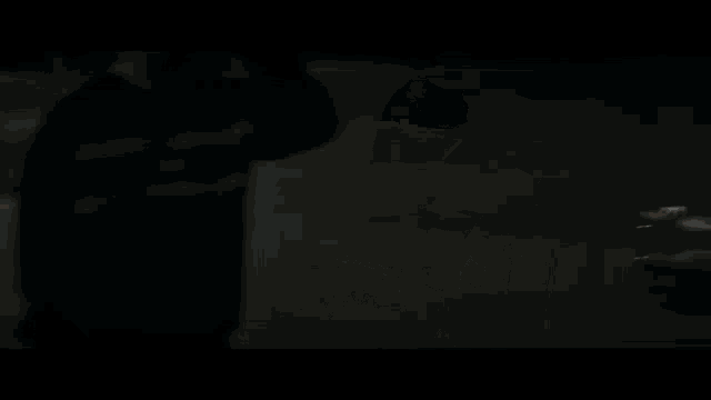 a man is holding a sword in a dark room while another man looks on .