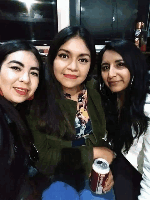 three women posing for a picture with one holding a coke can