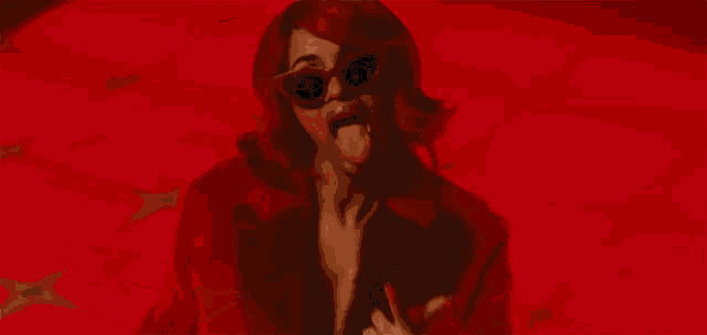 a woman wearing sunglasses and a red coat is sticking her tongue out