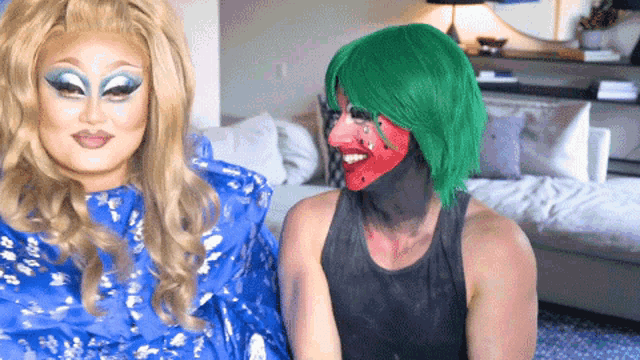 two drag queens are sitting next to each other with one wearing a green wig