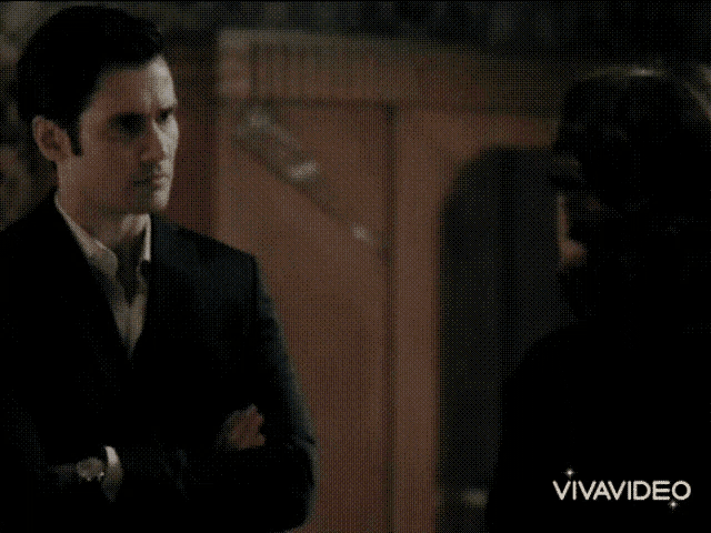a woman in a black dress is standing in front of a man in a room in a vivavideo video