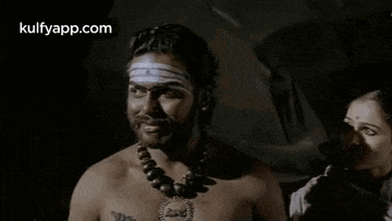 a man without a shirt is wearing a necklace and smiling while standing next to a woman .