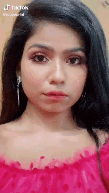 a woman wearing a pink top and earrings has a tiktok watermark on her face