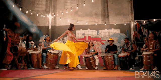 a woman in a yellow skirt is dancing in front of drums and the word bravas is on the bottom