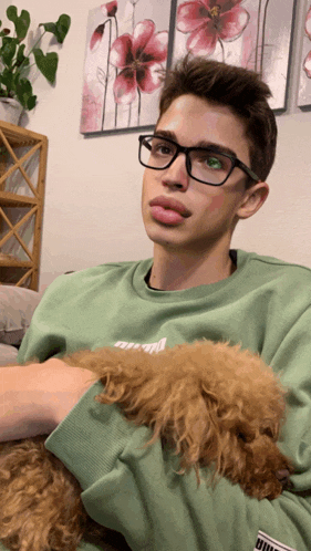 a young man wearing glasses holds a small brown dog in his lap