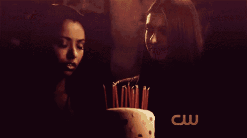 two women blowing out candles on a cake with the cw logo in the background