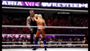 a man and a woman are in a wrestling ring with a sign that says mania