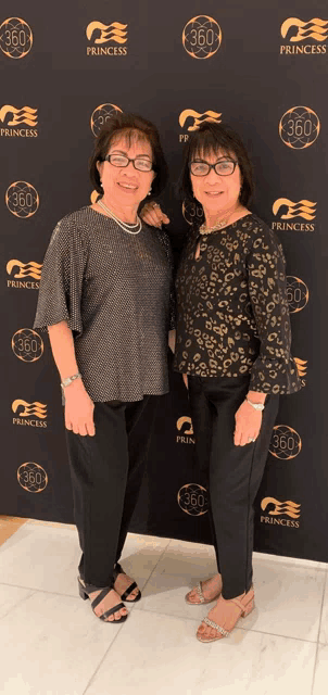two women standing in front of a princess 360 backdrop