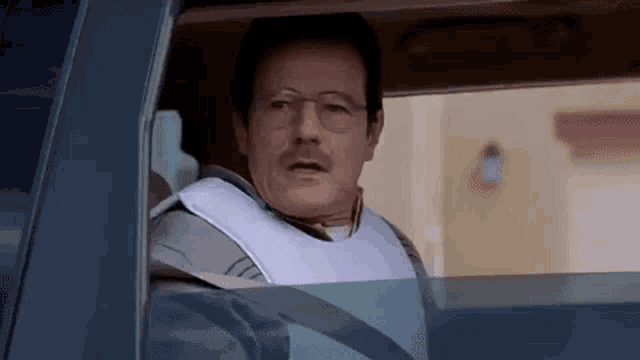 a man wearing glasses and a bib is driving a car .