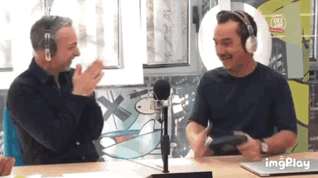 two men wearing headphones are sitting at a table in front of a microphone and a sign that says imgplay on it