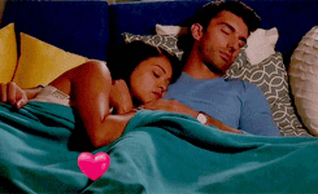 a man and a woman are sleeping in a bed with a heart on the blanket