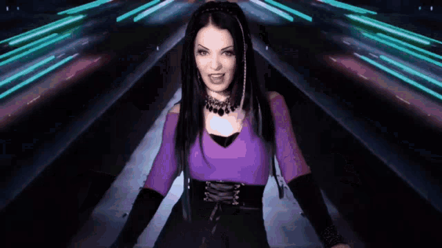 a woman in a purple top is standing in a dark room with neon lights behind her