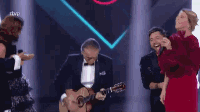 a man in a tuxedo is playing a guitar in front of a group of people with the letters rtve on the bottom