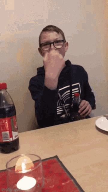 a boy is sitting at a table with a bottle of coca cola in the background