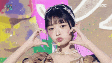a girl wearing sunglasses and a pearl necklace is making a heart shape with her hands