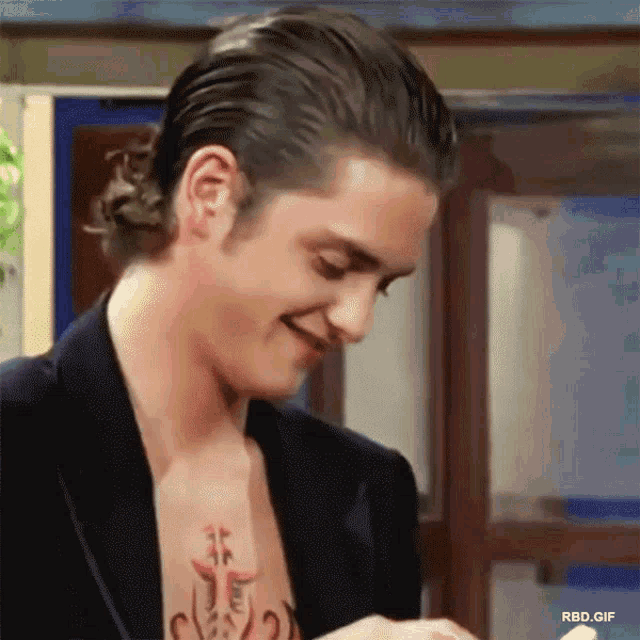 a man with a tattoo on his chest is smiling while wearing a suit jacket