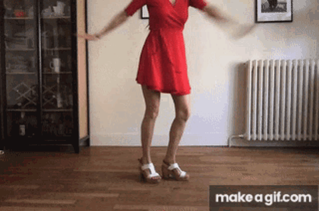 a woman in a red dress and white shoes is dancing in a living room