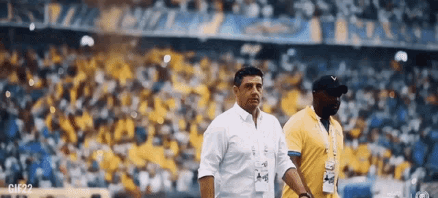 a man in a white shirt and a man in a yellow shirt are walking on a soccer field