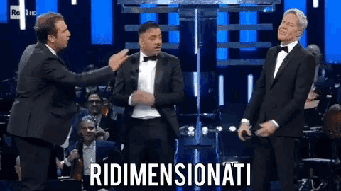 three men in tuxedos are standing in front of an orchestra with the word ridimensionati written on the bottom