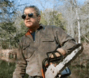 a man wearing sunglasses is holding a chainsaw in a field .