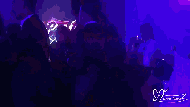 a group of people are dancing in a dark room with a sign that says cora alexa
