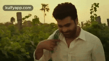 a man in a white shirt is standing in a field with a green cloth around his neck .