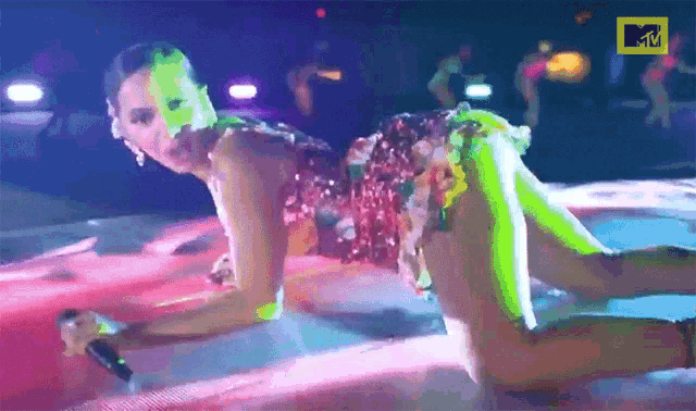 a woman is kneeling on the floor holding a microphone with a mtv logo in the background