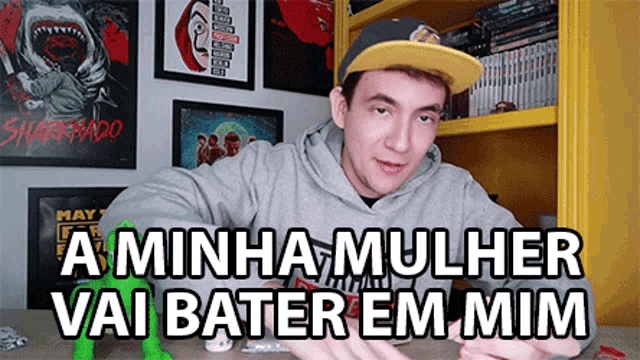 a man wearing a hat is sitting at a table with the words a minha mulher vai bater em mim in front of him