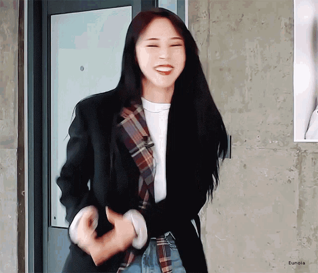a woman wearing a plaid shirt and a black jacket is standing in front of a door .