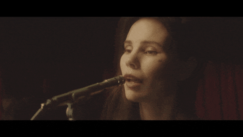a close up of a woman singing into a microphone with a tattoo on her face