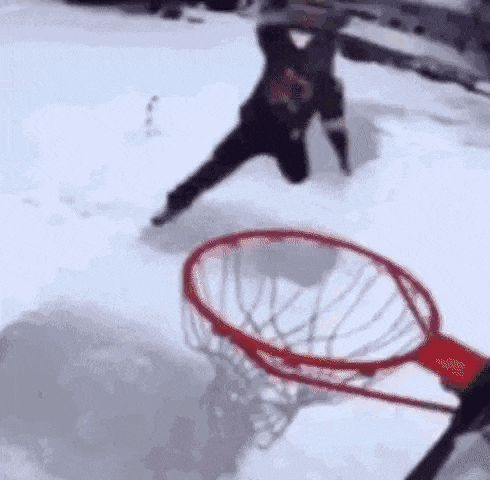 a man is playing basketball in the snow with a basketball hoop in the background .