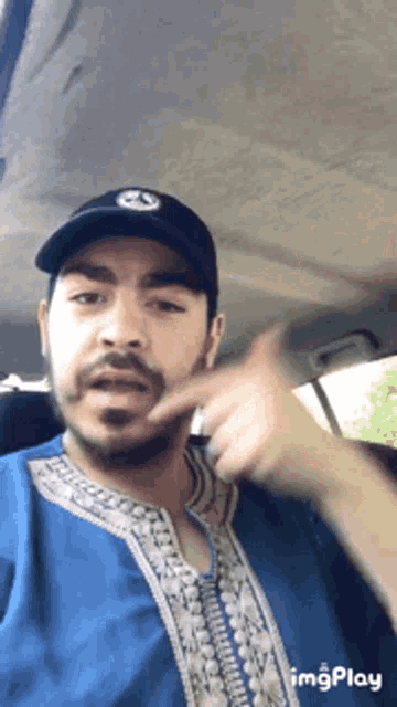 a man wearing a blue shirt and a black hat is making a gesture with his finger