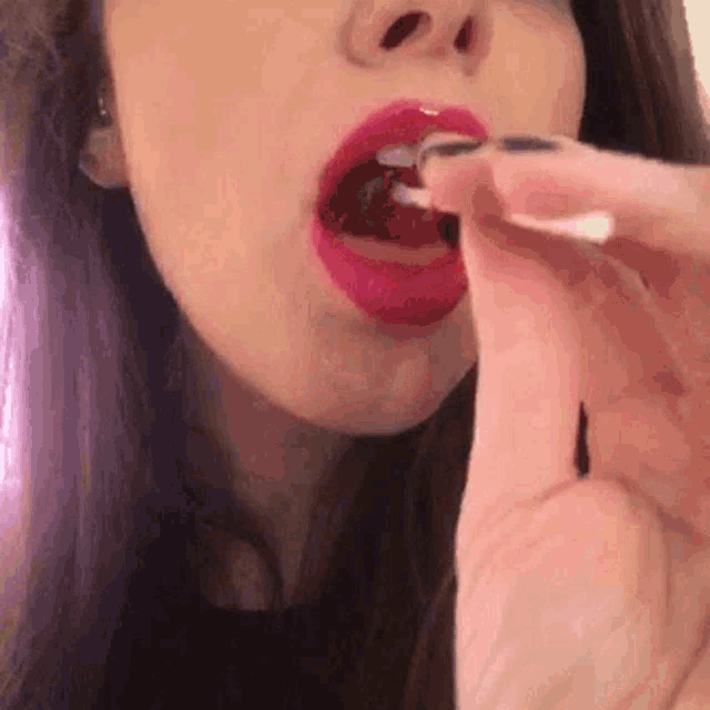 a close up of a woman 's mouth with red lipstick and black nails eating something .