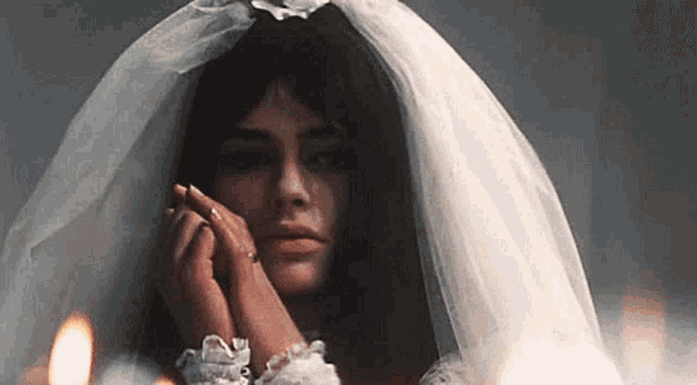 a woman in a wedding dress and veil is crying while standing in front of a fire .
