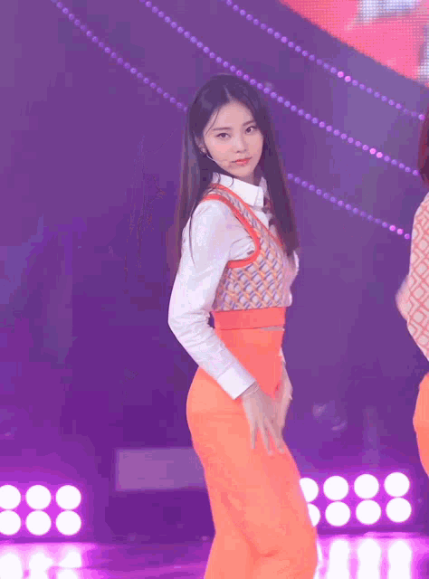 a woman in a white shirt and orange pants is standing in front of a purple background