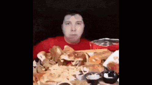 a man in a red shirt is sitting at a table eating french fries and a hamburger .