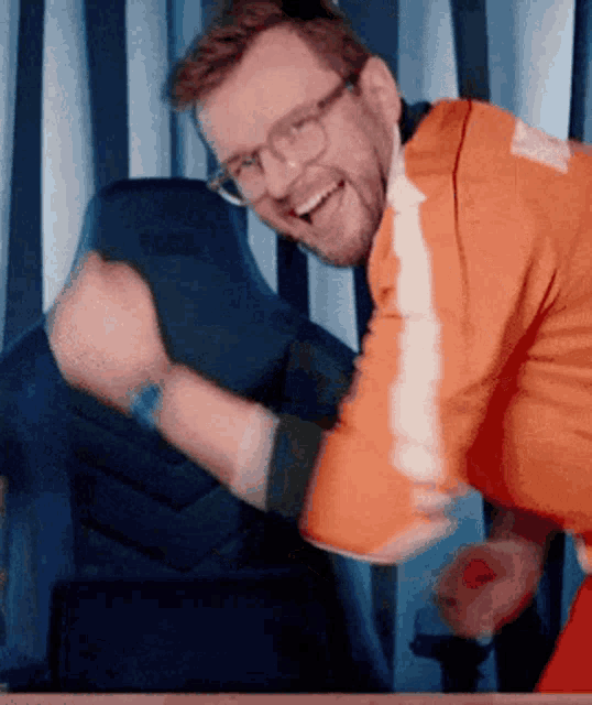 a man wearing glasses and an orange jacket is laughing with his hands in the air