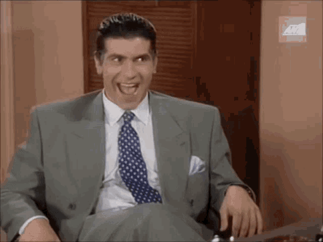 a man in a suit and tie is laughing while sitting in front of a sign that says avh