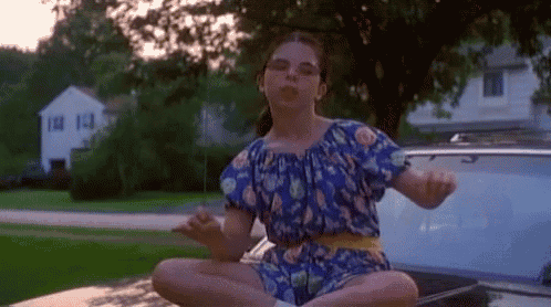 a young girl in a blue dress is sitting on the back of a car in a lotus position .