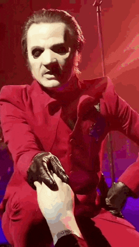 a man in a red suit and gloves is kneeling down and holding a person 's hand .