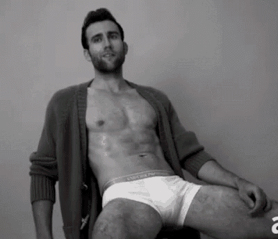 a shirtless man is sitting on a chair wearing white underwear and a cardigan .