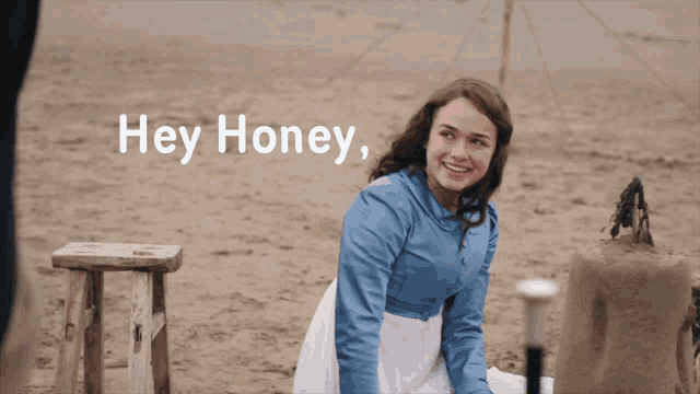 a woman in a blue shirt sits on the beach with the words hey honey above her