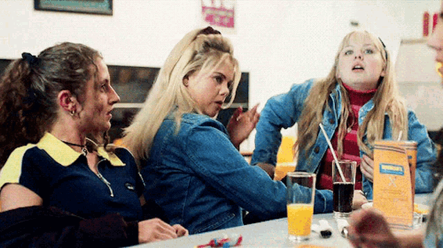 a group of girls are sitting at a table with a box of orange juice in front of them