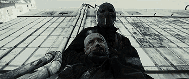 a man in a mask is holding another man 's head with the words bakmasenoni.org written below him