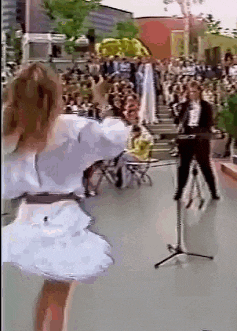 a woman in a white dress is dancing in front of a microphone in front of a crowd of people .