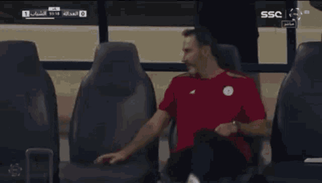 a man in a red shirt sits in a soccer stadium watching the game