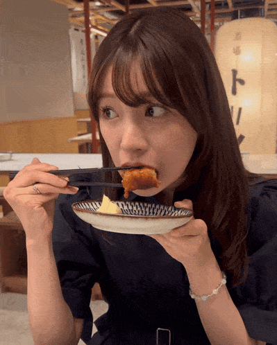 a woman is eating a piece of food from a plate with chopsticks in her mouth