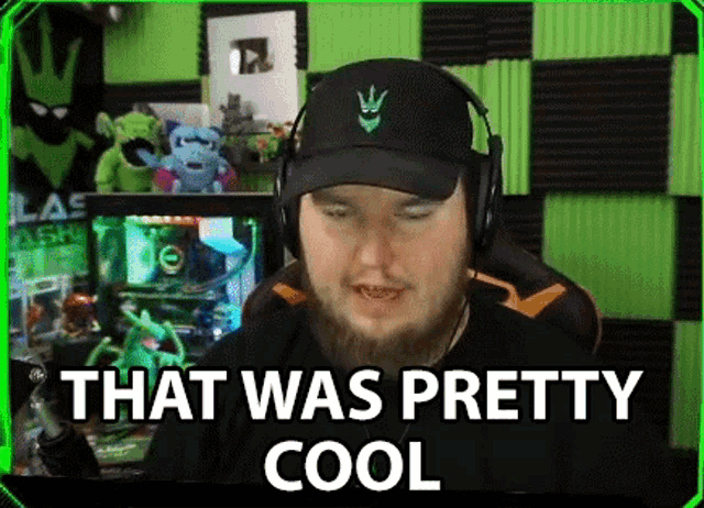 a man with a beard wearing headphones and a hat is sitting in front of a computer screen .